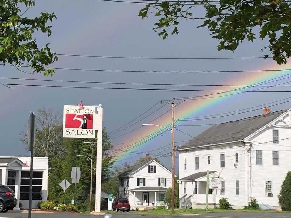 Rainbow arches over Station 51 Salon sign and houses, with trees in the foreground.