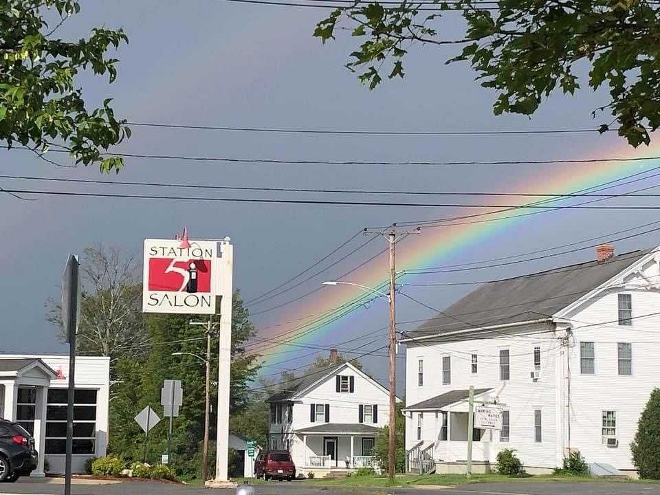 Rainbow arches over Station 51 Salon sign and houses, with trees in the foreground.
